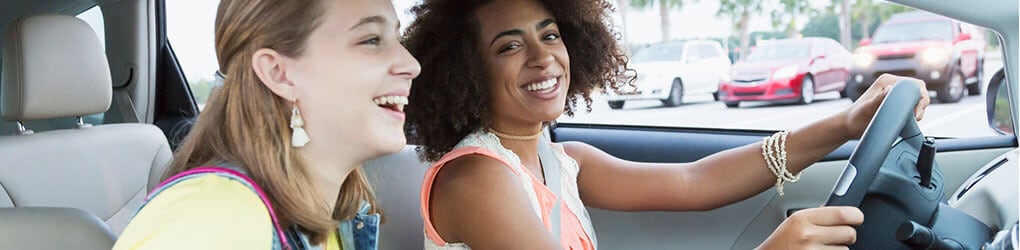 two teenagers in a car laughing and looking away from the road