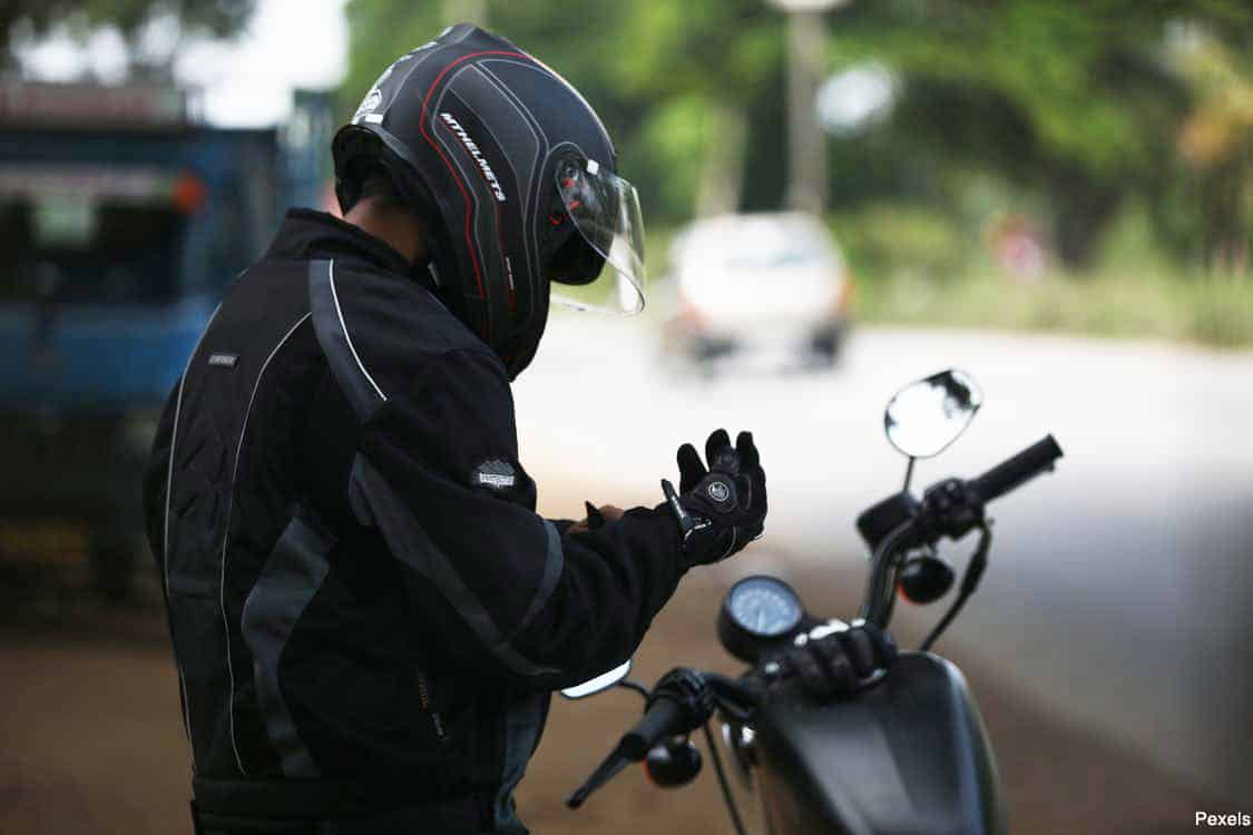 motorcyclist wearing a helmet and standing next to their bike fixing their glove