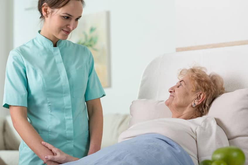 Nurse standing at elderly woman's bedside