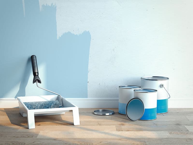 Paint cans and paint roller brush near light blue walls, 2 cans are opened, 1 is closed