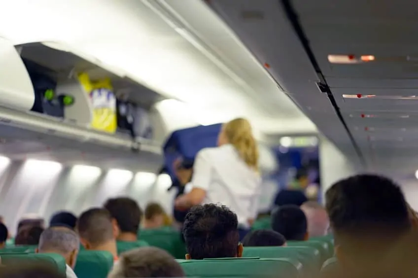 a flight attendant lifting luggage into the overhead compartment in the cabin of an airplane filled with passengers