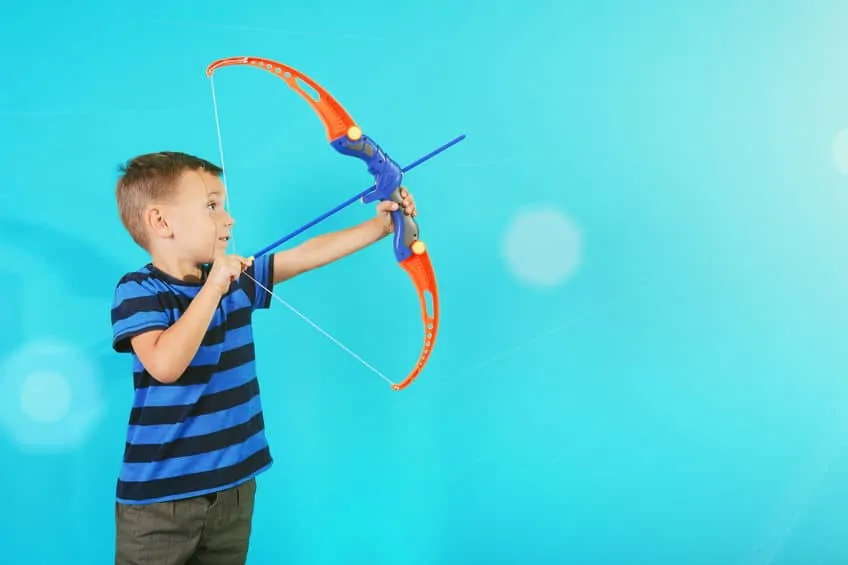 boy shooting a toy bow and arrow against a blue background