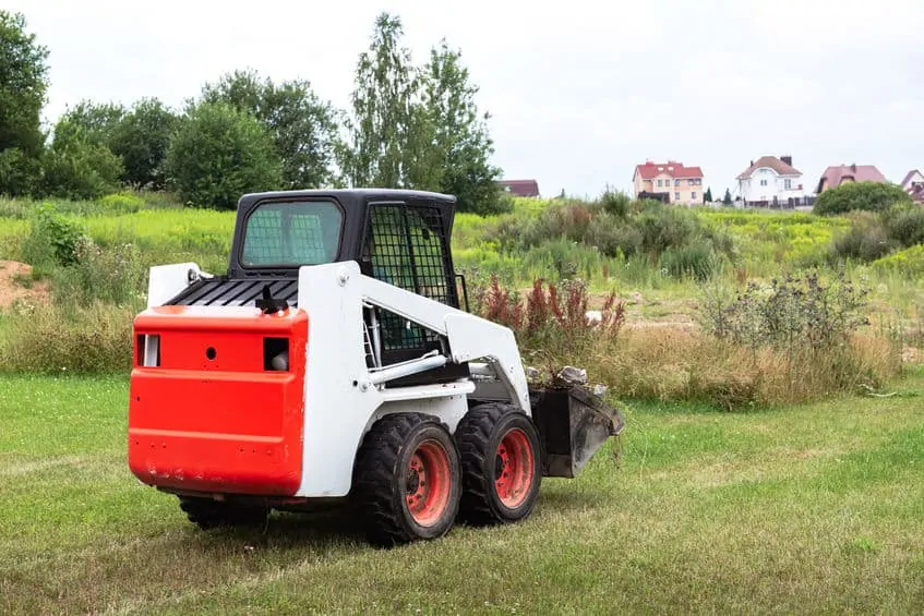 A skid steer loader clears the site for construction. Land work by the territory improvement. Machine for work in confined areas. Small tractor with a bucket for moving soil, turf and bulk materials.
