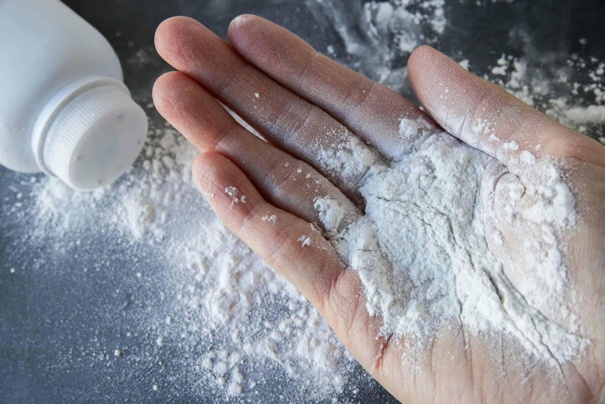 talcum powder on a hand, with a spilled bottle of talcum powder or baby powder in the background over a black table