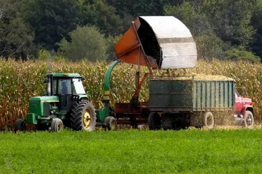 tractor and other farming equipment being run next to a corn field