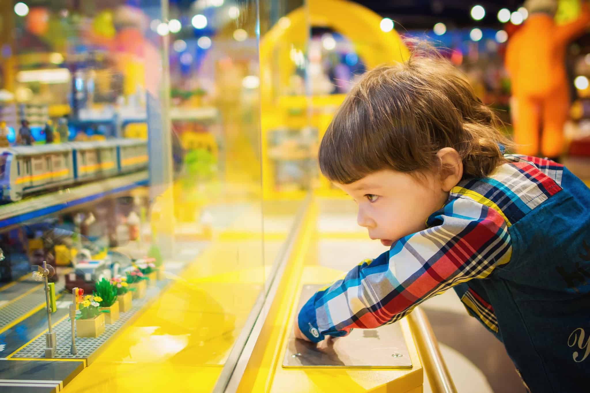 child looking at small toys through a glass wall