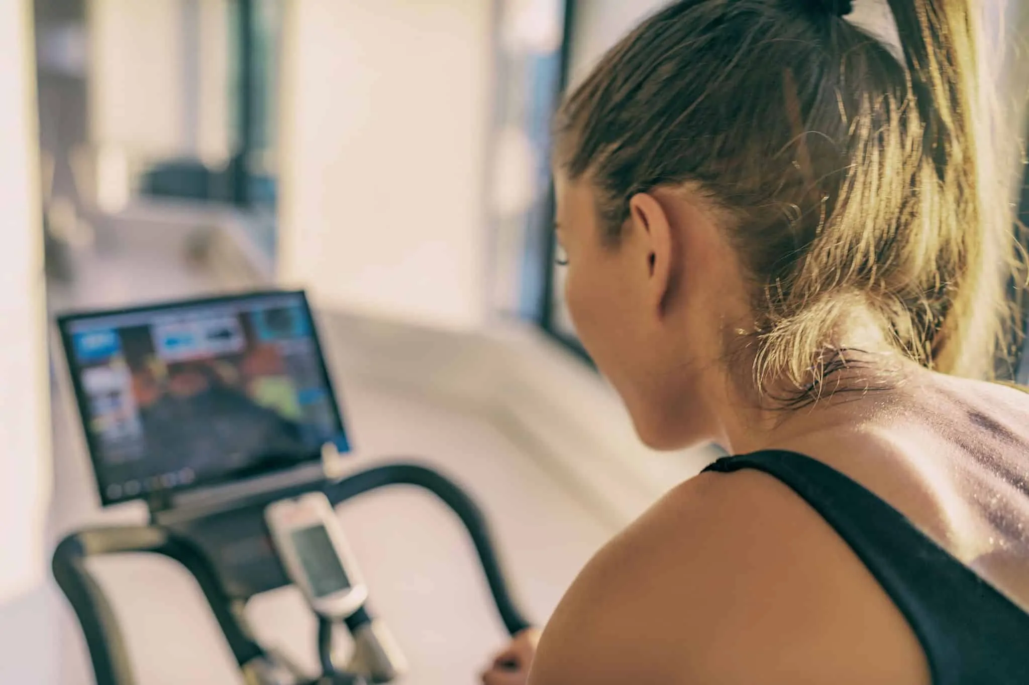 Smart fitness home workout biking screen with online classes woman training on stationary bike equipment indoors for biking exercise. Indoor cycling. Focus on the sweat on person's back.