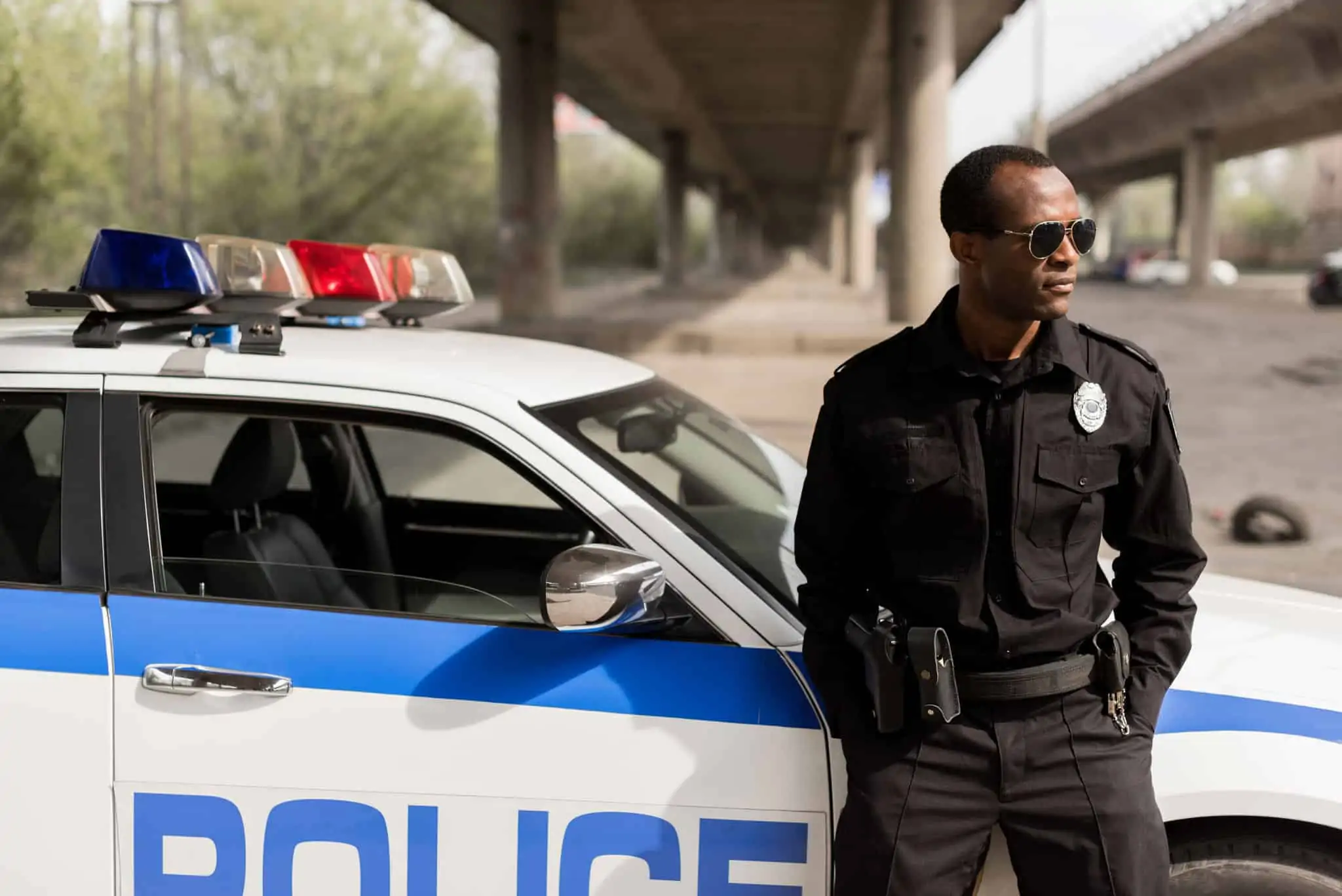 african american police officer leaning back on car and looking away